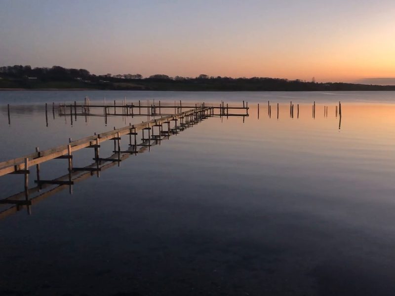 A wooden dock reaching out over still water at sunset