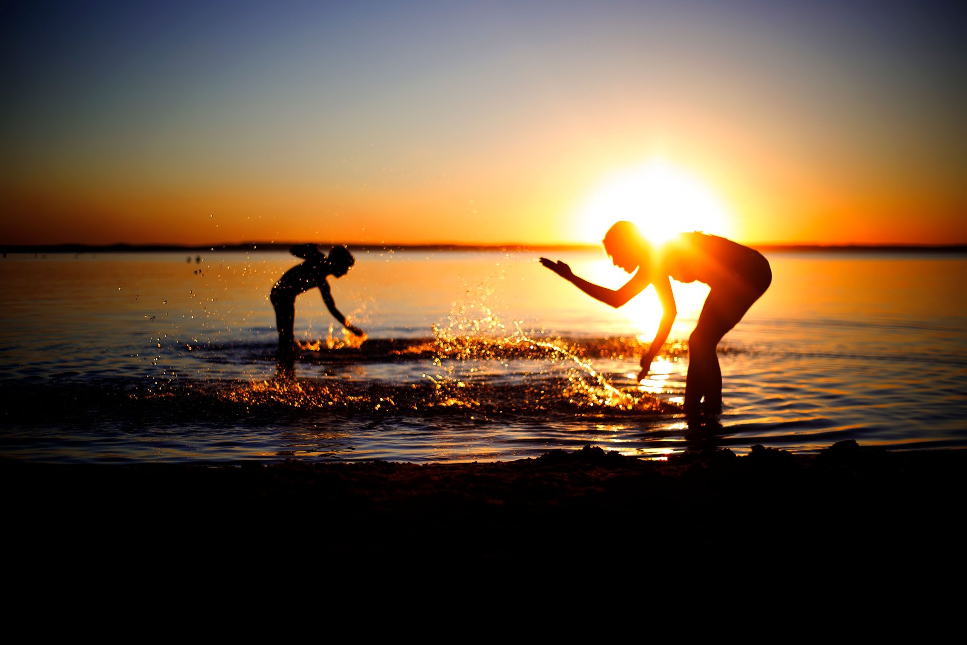 Two figures playing in the water at sunset, splashing golden light